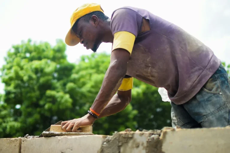Builder laying concrete blocks on a fresh bed of mortar on an outdoor building site