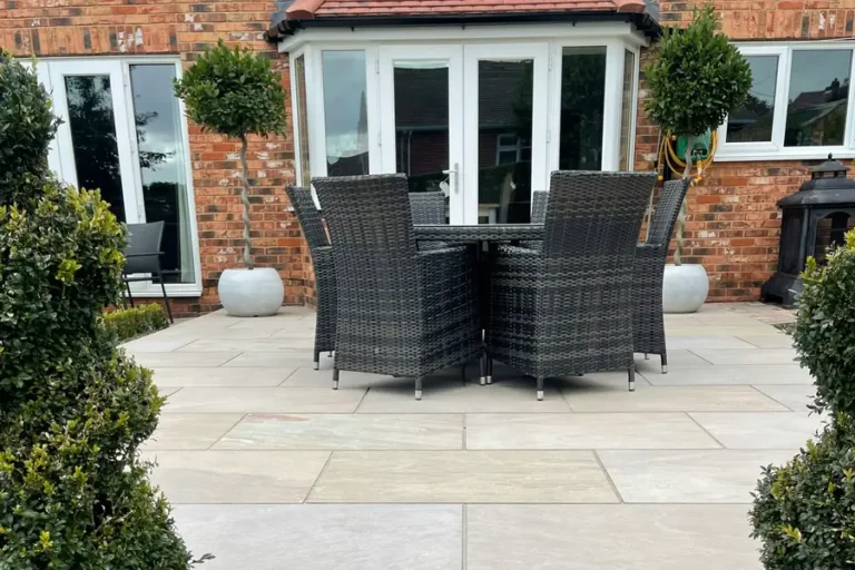 Newly laid sandstone patio with rattan garden furniture and clipped topiary behind a red-brick UK home
