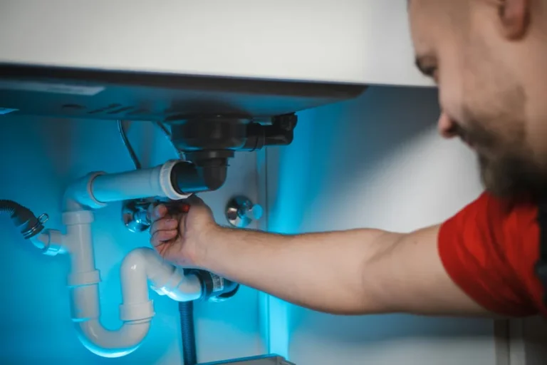 Plumber tightening the waste trap and pipework under a bathroom sink