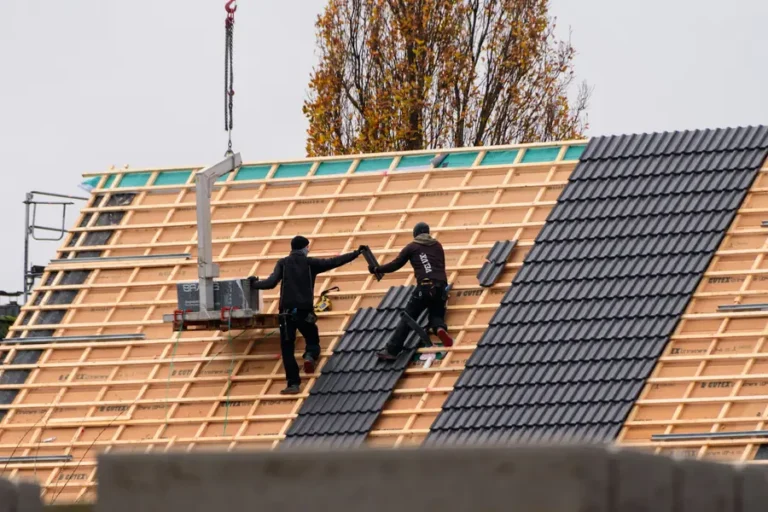 Two roofers laying dark concrete roof tiles over new timber battens and breathable membrane on a pitched roof