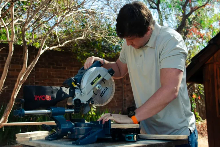 Tradesman cutting timber on a sliding mitre saw in a garden with a red-brick wall behind